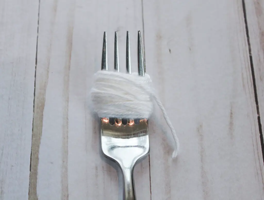 wrap yarn arounf tines of fork to create pom pom